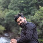 Portrait of an Indian man wearing a black shirt by a lush riverside in Nilambur, Kerala.